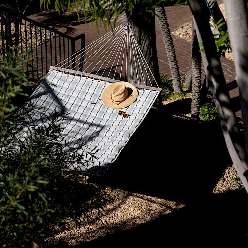 A hammock is set up among trees, with a straw hat casually placed on it, suggesting a relaxed outdoor setting.