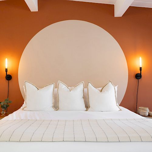 A modern bedroom with an orange wall and a large circular accent, featuring a bed with four pillows and two wall-mounted lights on each side of the bed.