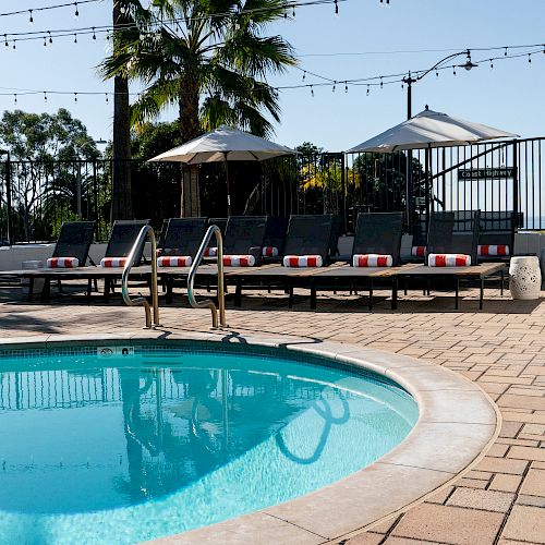 The image shows a serene outdoor pool area with lounge chairs and umbrellas, set under string lights, with a palm tree in the background ending the sentence.