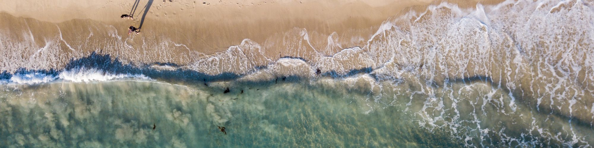 Aerial view of a beach with people walking along the shore and several swimmers in the clear turquoise water.